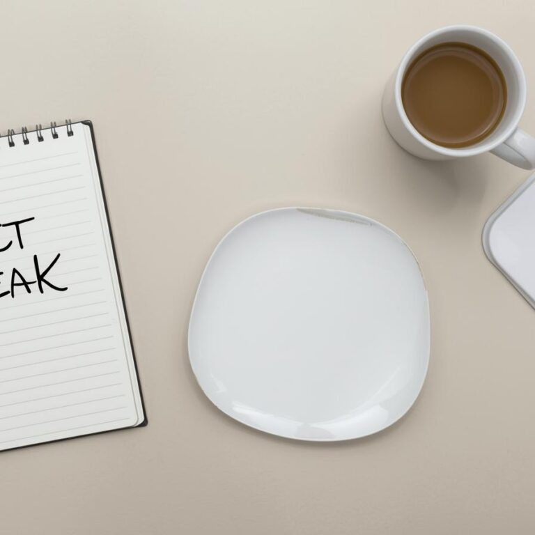 Flatlay lumineux sur table beige avec carnet ouvert “Diet Break”, assiette équilibrée, tasse de café fumant, montre et plante verte — symbolisant la planification et l’équilibre dans une perte de poids durable.